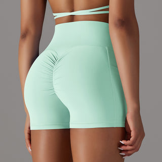 Mint-colored high-waisted sports shorts with a phone pocket design, modeled on female figure against a gray background.