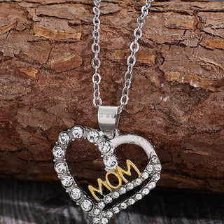 Elegant crystal heart-shaped pendant necklace with "Mom" text and silver-toned chain on a wooden background.