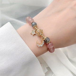 Colorful natural stone star and moon charm bracelet adorned with strawberry quartz crystals and gold-tone metal elements, on a woman's wrist against a white background.