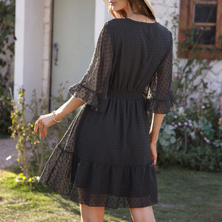 Elegant black lace midi dress with voluminous sleeves and ruffled hemline, set against a nature-filled garden backdrop.