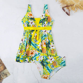 Vibrant tropical-print women's halter-style bikini and swimsuit with pineapple and floral designs, displayed on a minimalist white background with seasonal accessories.
