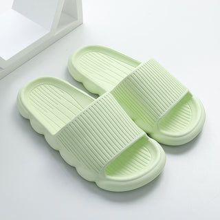 Soft green women's home slippers with a wavy, textured design on a white background.