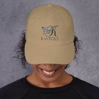 Stylish beige dad hat with K-AROLE logo, worn by smiling person with curly hair against a gray background.