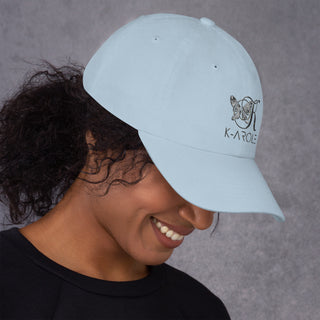 Stylish white dad hat with K-AROLE logo, worn by a smiling woman with curly hair against a gray background.