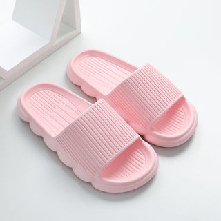 Soft pink women's home slippers with wavy non-slip soles, displayed on a white background with a mirrored surface.