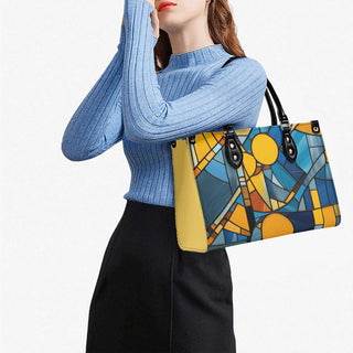 Stylish woman's tote bag with abstract stained glass pattern in vibrant yellow and blue hues, carried by a woman wearing a cozy blue ribbed sweater.